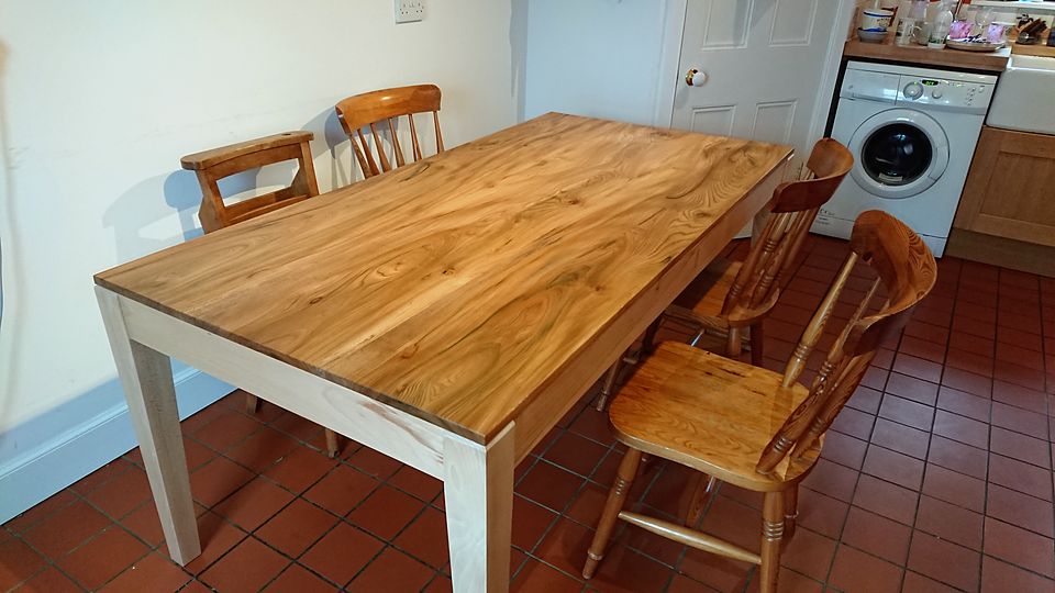 Dining table with a figured plank top and pale square legs, in a tiled kitchen