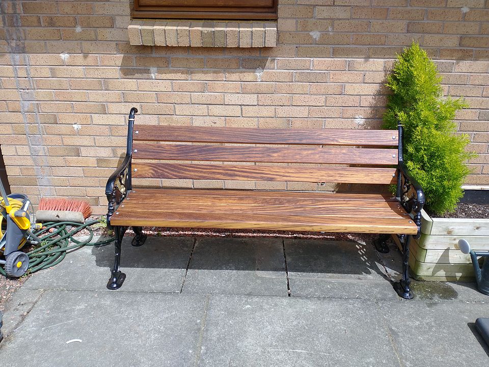 Garden bench with cast iron ends and new hardwood slats, against a brick wall